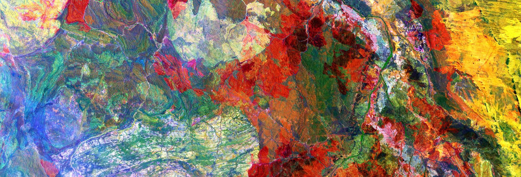 False-color satellite image of cultivated highland terrain, scarlet and ochre fields breaking against pale drainage.